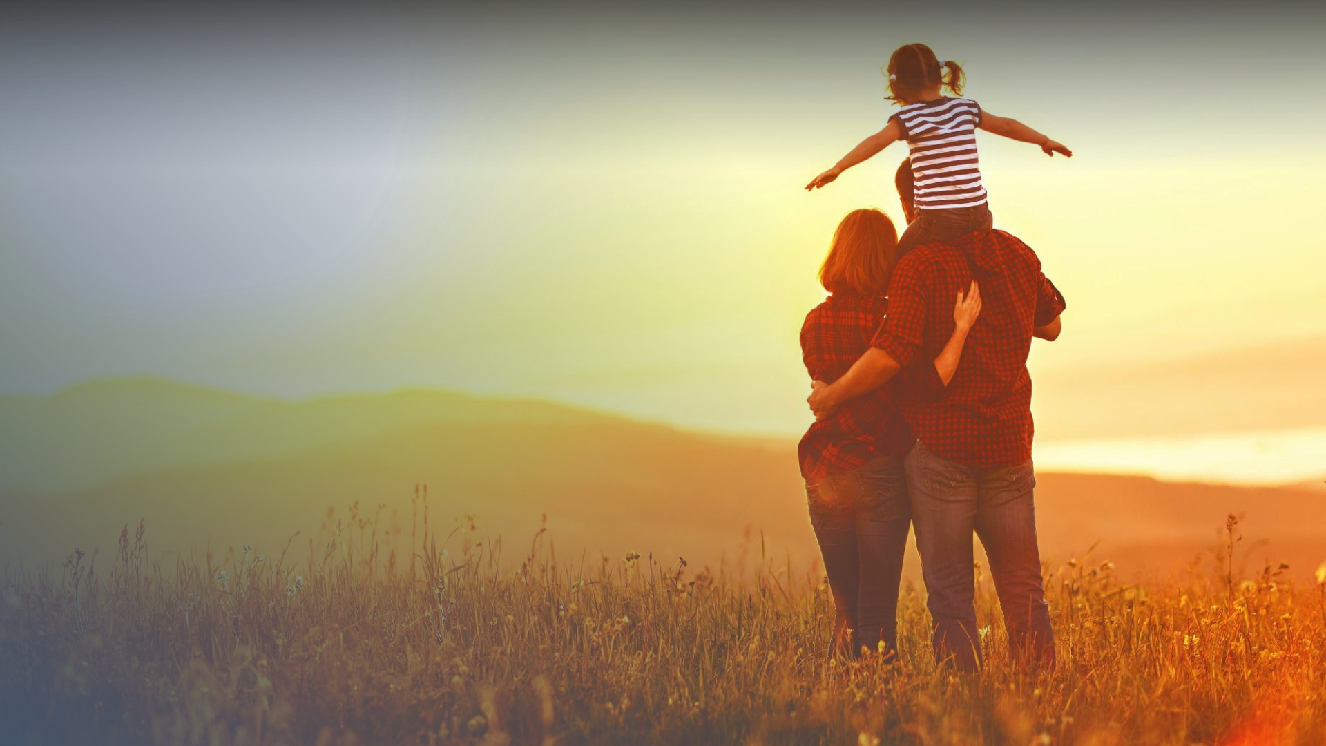 Mother and father standing, child on father's shoulders watching sunset