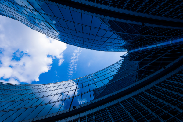 view from below of two windowed buildings converging with blue skies above
