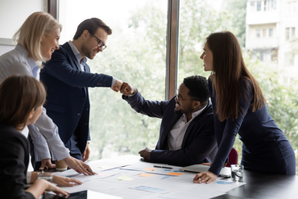 Diverse professionals around table, two fist-bumping