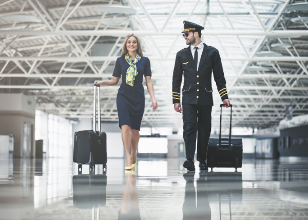 pilot and flight attendant dressed for work with suitcases walking through airport