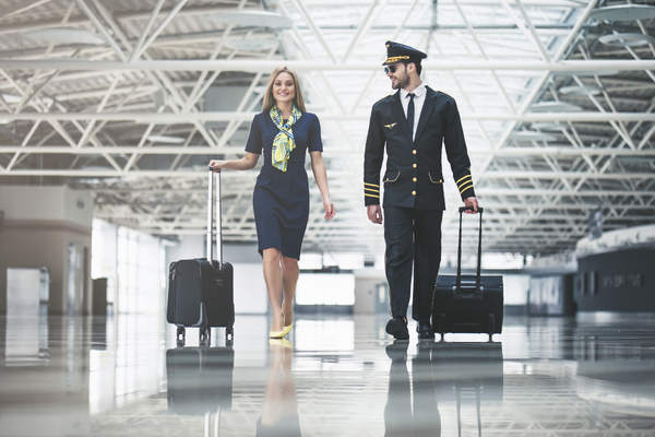 pilot and flight attendant dressed for work with suitcases walking through airport