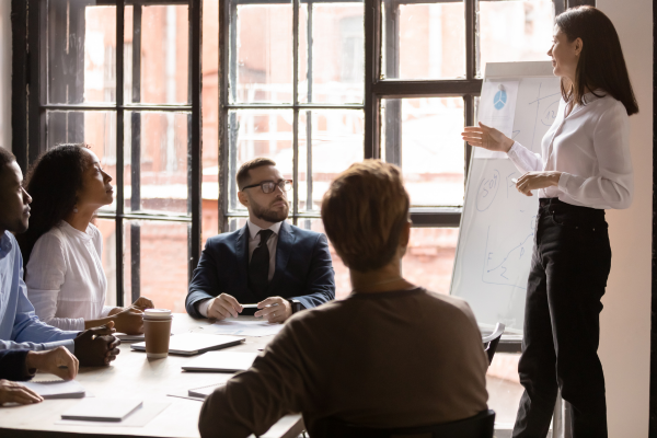 small group of people seated at table watching woman speak with graphs