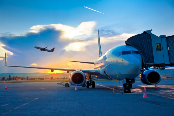 airplane on ground with boarding bridge and a plane taking off in background 