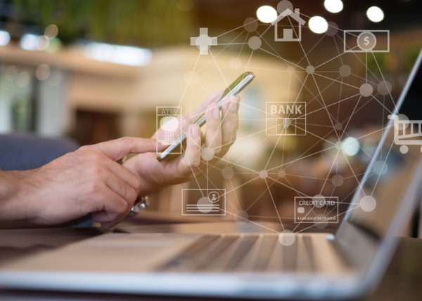 hands holding a cell phone in front of a laptop with virtual banking icons