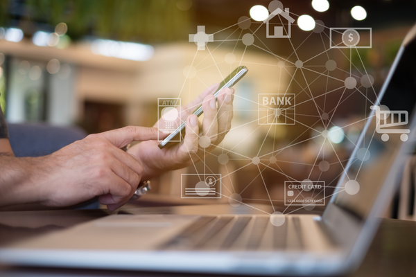hands holding a cell phone in front of a laptop with virtual banking icons