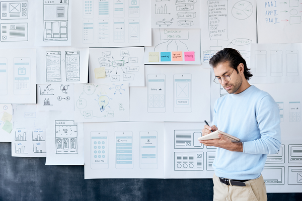 person writing in notebook with UX sketches in background