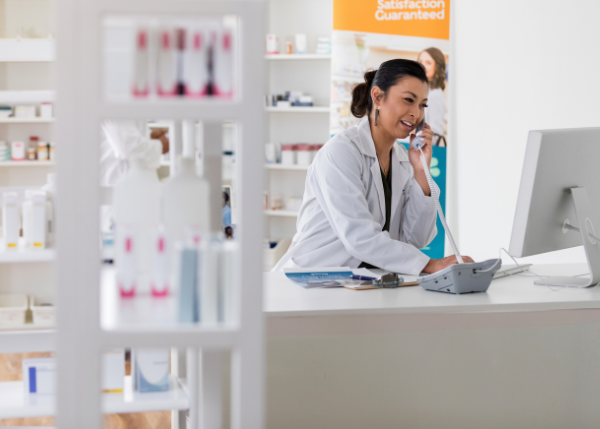 woman in retail pharmacy wearing lab coat on a landline phone