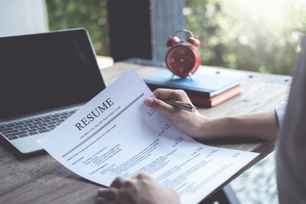 Hands holding paper resume in front of laptop and desk