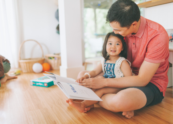 Father reading book to toddler daughter in lap