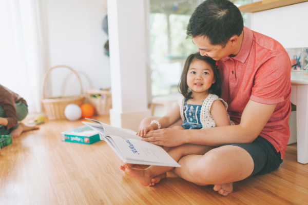Father reading book to toddler daughter in lap