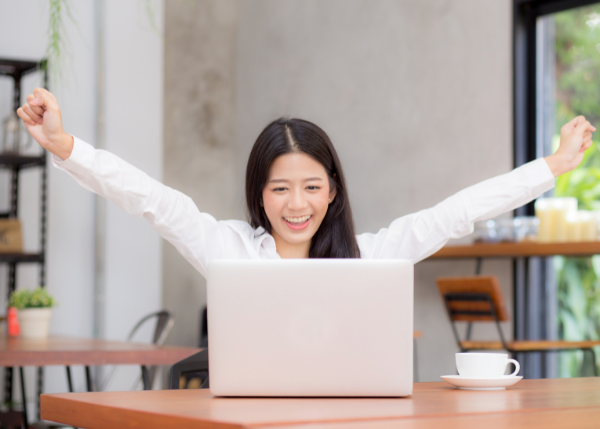 Asian women smiling in front of laptop and arm raised