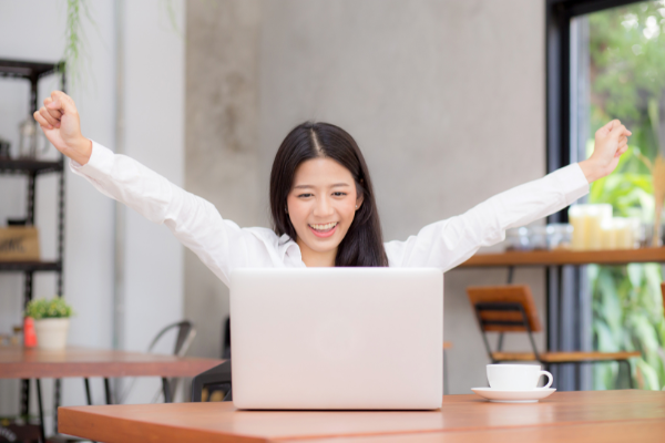 Asian women smiling in front of laptop and arm raised