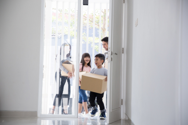 Parents and two children smiling, carrying moving boxes, entering vacant apartment