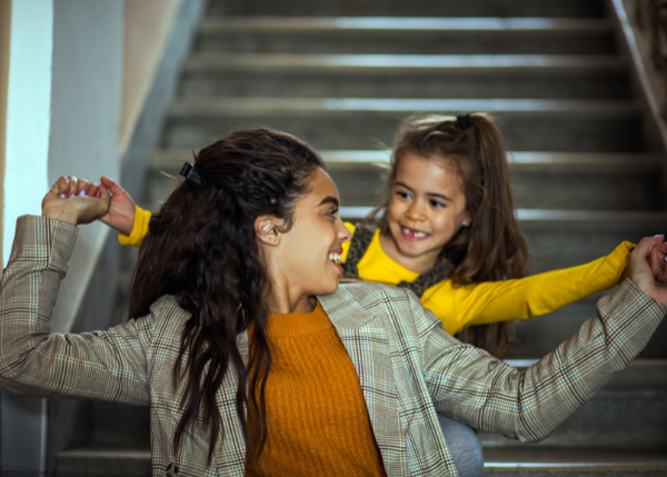 Young mom and daughter sitting on stairs, holding hands and smiling