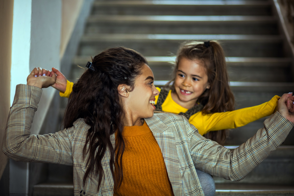 Young mom and daughter sitting on stairs, holding hands and smiling