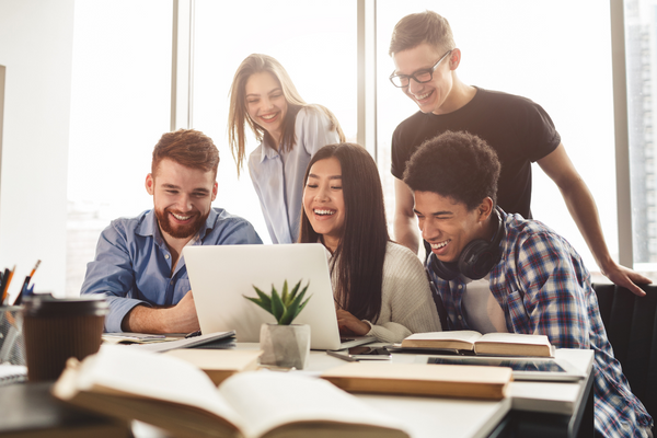 Young diverse adults smiling and looking at laptop around desk