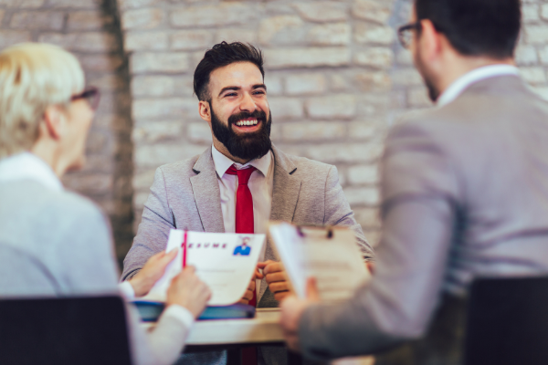 Two professionals seated at table interviewing smiling businessman crew cut