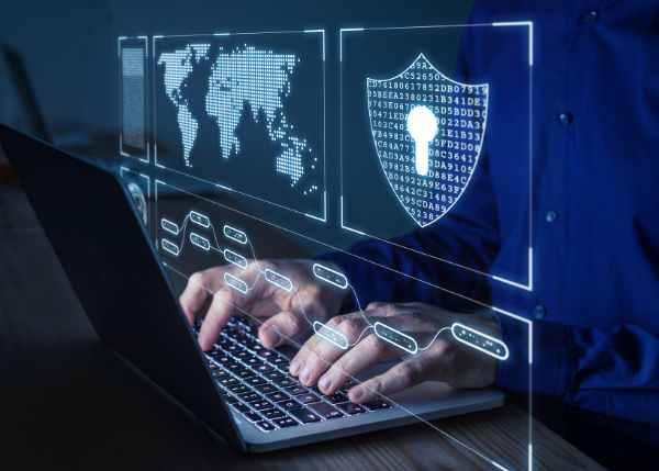 Hands typing on a laptop with cybersecurity graphics floating above