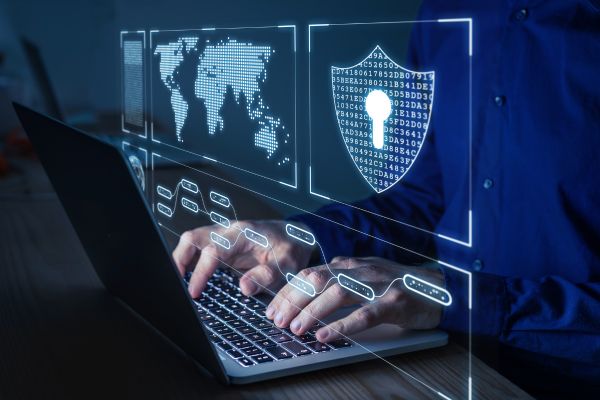 Hands typing on a laptop with cybersecurity graphics floating above