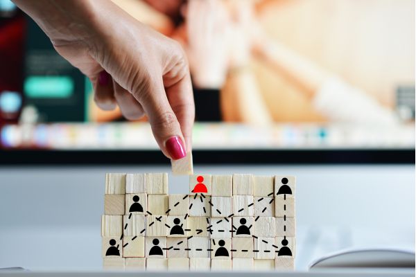 a hand placing a block on a stack of blocks with symbols representing organizational relationships