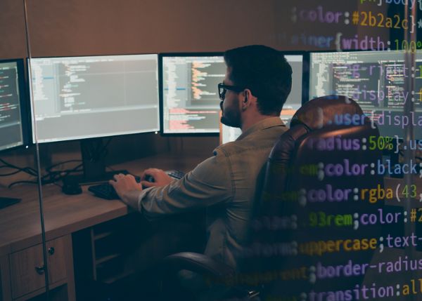 person seated in front of multiple screens with code 