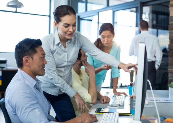 woman standing next to a man pointing to something on his computer