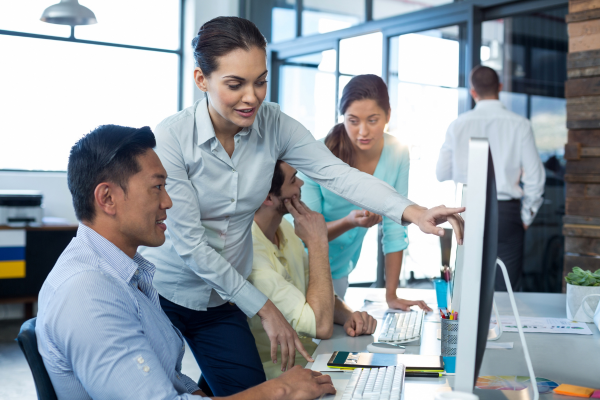 woman standing next to a man pointing to something on his computer