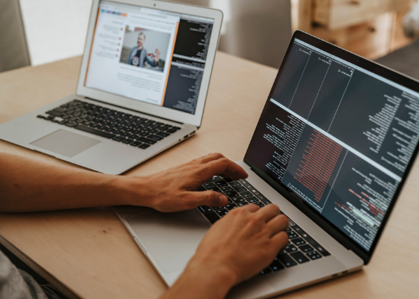 Two laptops, worker interacting with lines of code
