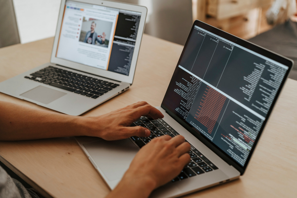 Two laptops, worker interacting with lines of code