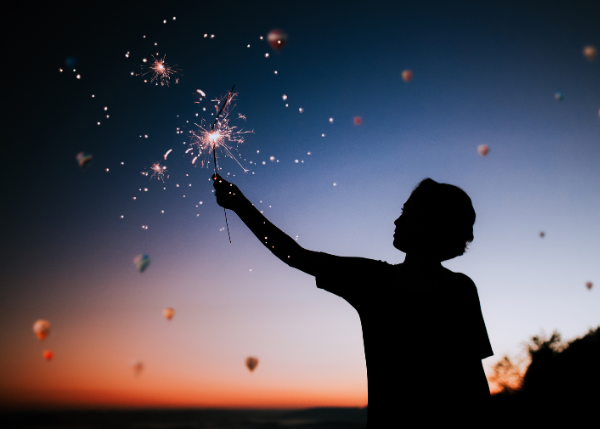 Person holding a sparkler with hot air balloons in the background