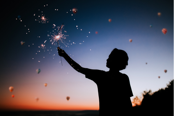 Person holding a sparkler with hot air balloons in the background