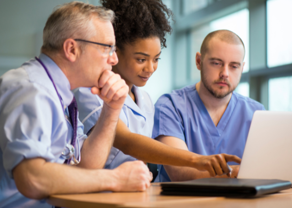 Medical workers gathered around a laptop that they are looking at.