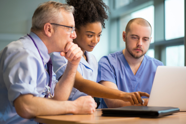 Medical workers gathered around a laptop that they are looking at.